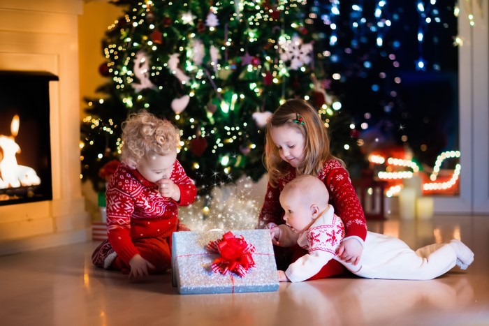 Three children opening a Christmas gift by the tree