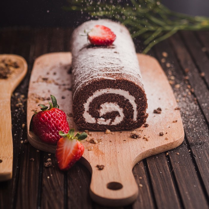 Chocolate Swiss roll with strawberries on a cutting board