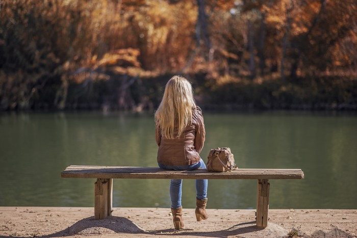 Blonde girl sitting on a bench by a lake in autumn