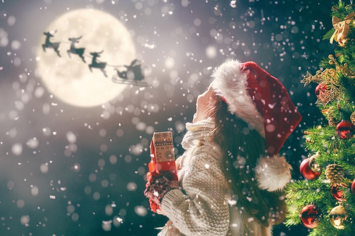 Girl in Santa hat watching Santa's sleigh fly by the moon