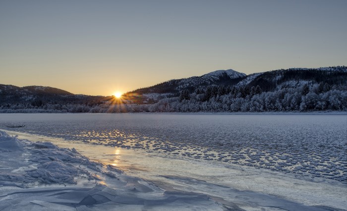 Sunrise over a frozen Namsen river in Norway with mountains and forests
