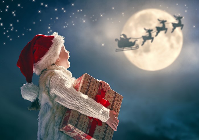 Child with Christmas gift looking at Santa's sleigh