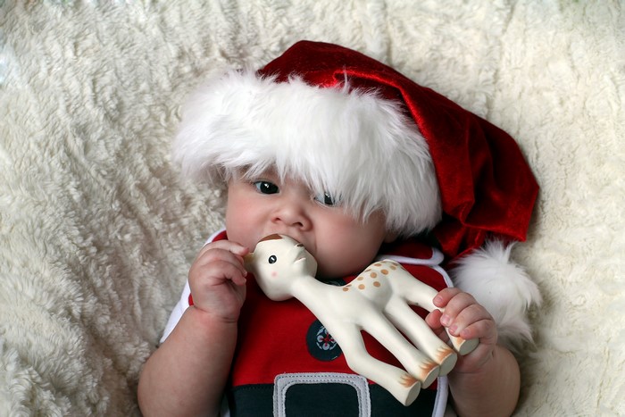 Baby in Santa hat chewing on a giraffe toy