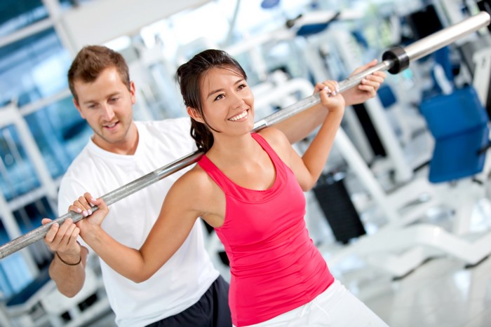 Man assisting woman with barbell in gym