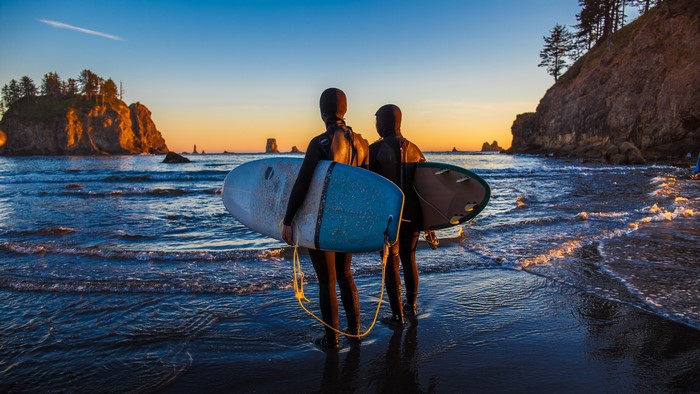 Two surfers with surfboards on the beach at sunset