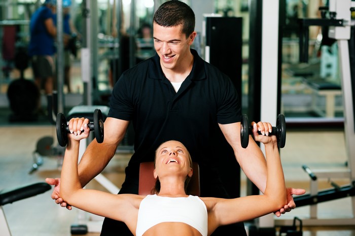 Fitness trainer assisting woman with dumbbells