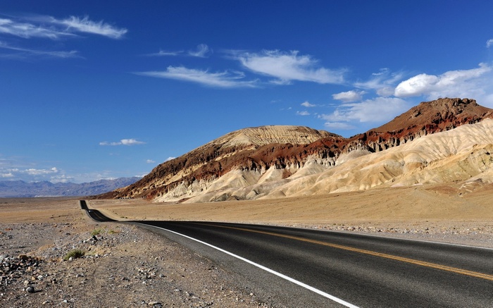Desert road leading to colorful mountains under blue sky