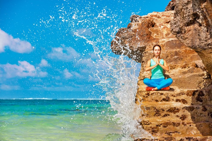 Woman meditating on rocks with ocean splash