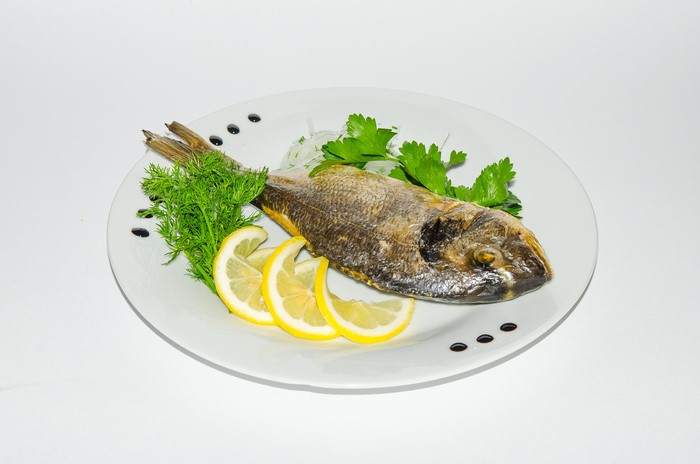Whole cooked fish with lemon and herbs on a plate