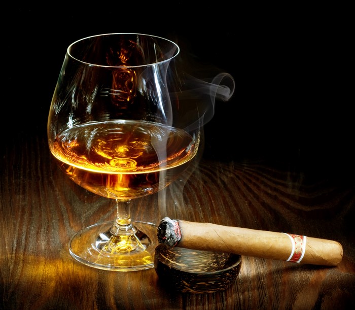 A glass of amber liquid and a smoking cigar