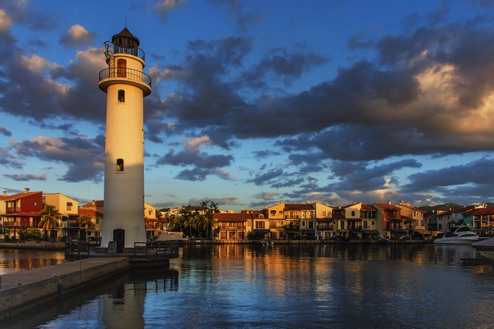 Lighthouse and houses by the river at sunset