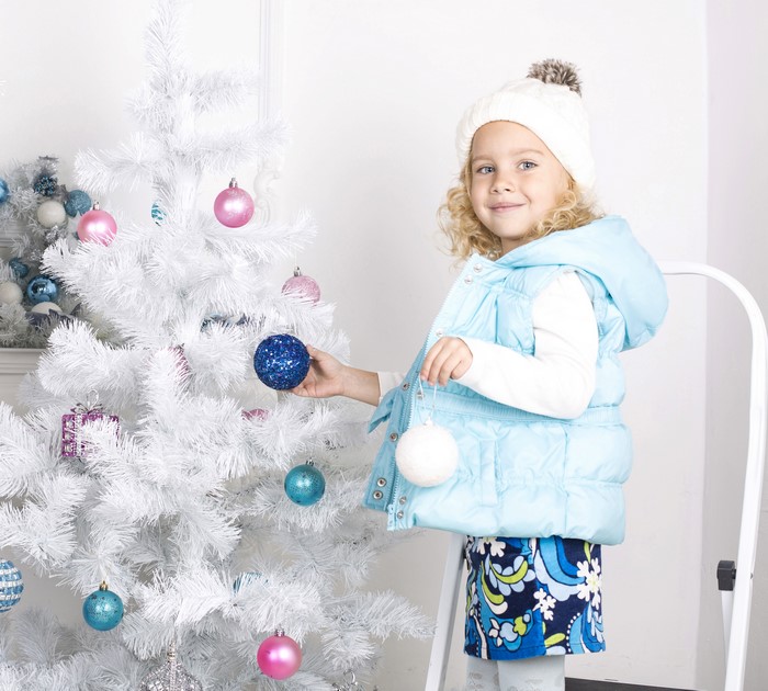 Girl decorating a white Christmas tree with ornaments