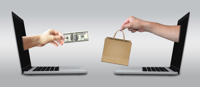 Hands exchanging money and shopping bag through laptops