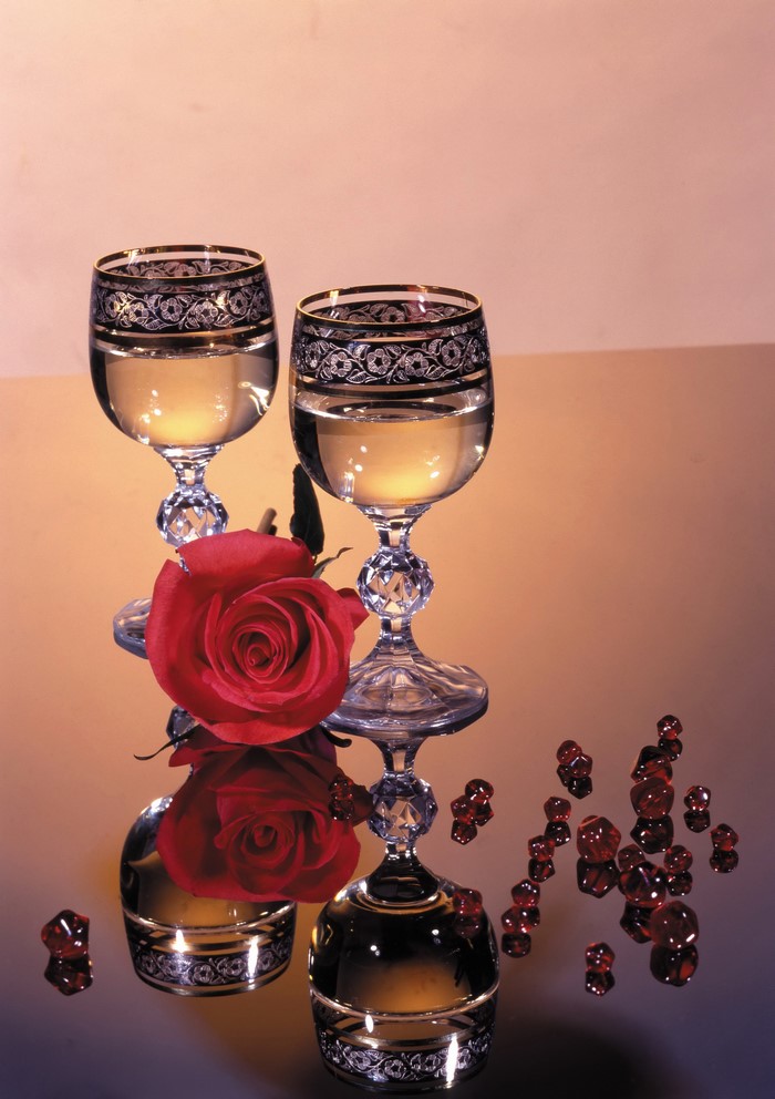 Two champagne glasses with a red rose and red gems