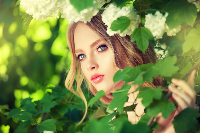 Beautiful woman with blue eyes and blonde hair among flowers and leaves