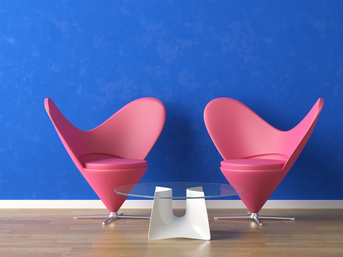Two pink armchairs and a glass table in front of a blue wall