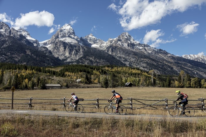 Cyclists ride past wooden fence with mountains in background