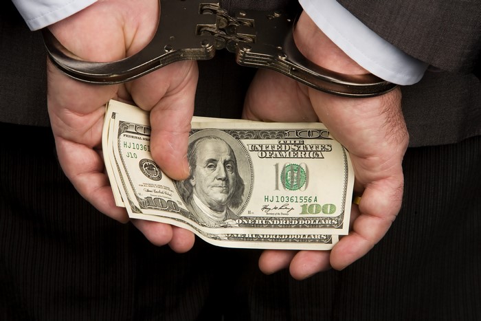 Handcuffed hands holding US dollar banknotes