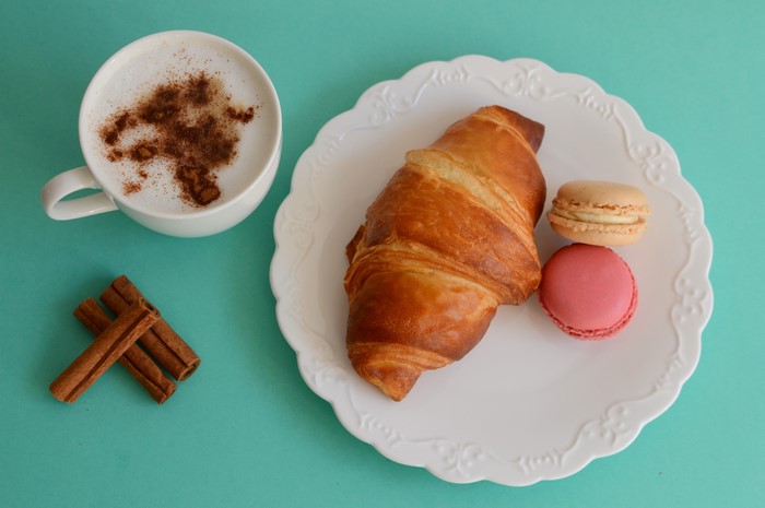 Cappuccino with cinnamon, croissant, and macarons on a plate