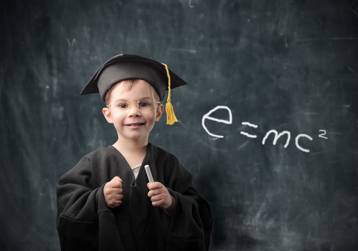 Boy in graduation gown and cap with e=mc2 on blackboard
