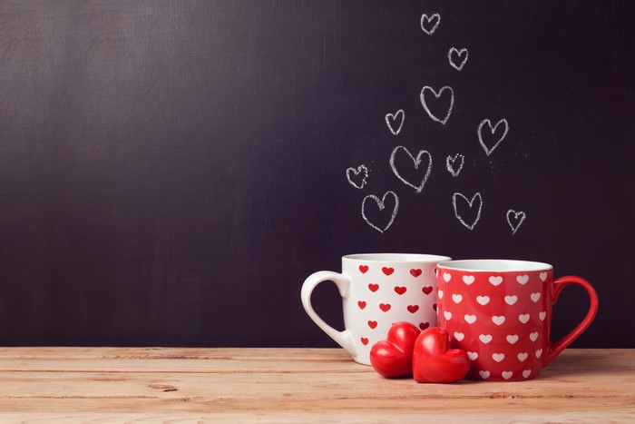 Two mugs with hearts and chalk hearts on blackboard