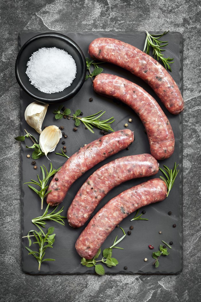 Raw sausages with garlic, salt, pepper, and herbs on a cutting board