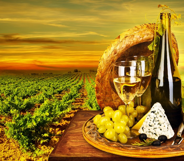 Wine, cheese, and grapes in a vineyard at sunset