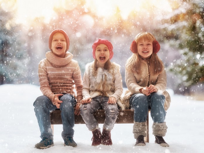 Three children sitting on a bench in the snow