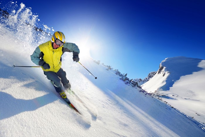 Man skiing down a snowy mountain under a bright sun