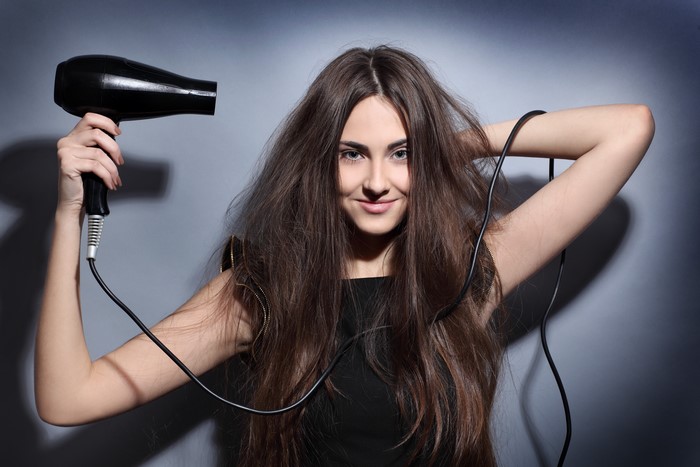 Woman with messy brown hair holding a hair dryer