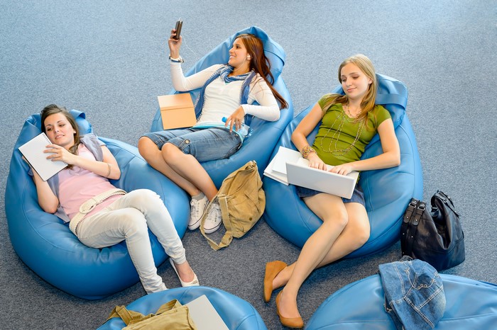 Three young women sitting on beanbag chairs with laptops and smartphones