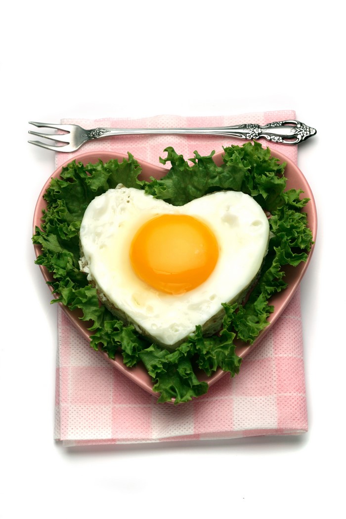 Heart-shaped fried egg on lettuce with fork