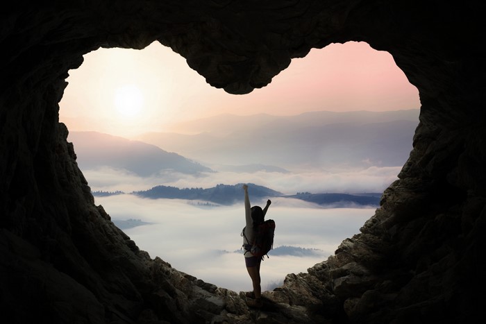 Hiker with arms raised in a heart-shaped cave opening