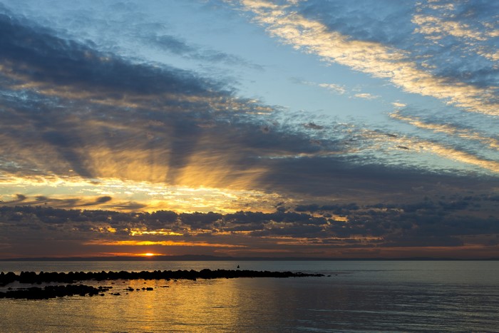 Sunset over the ocean with dramatic clouds and rock formations