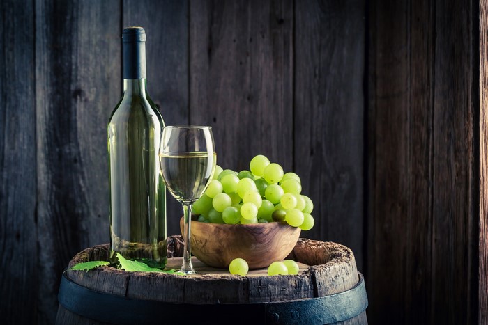 White wine bottle, glass, and grapes on a barrel