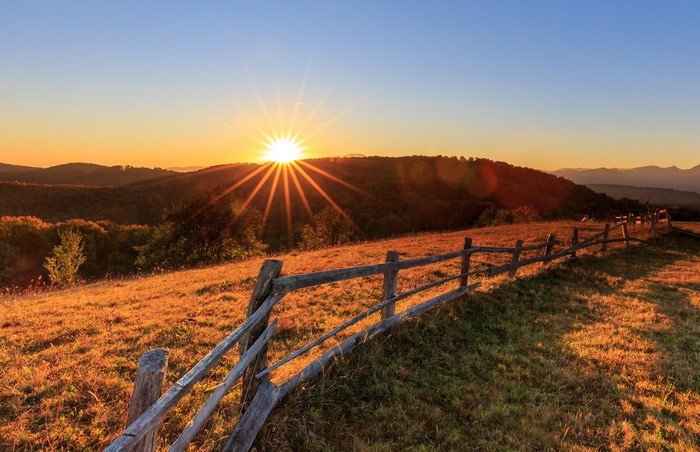 Sunrise over rolling hills with a wooden fence