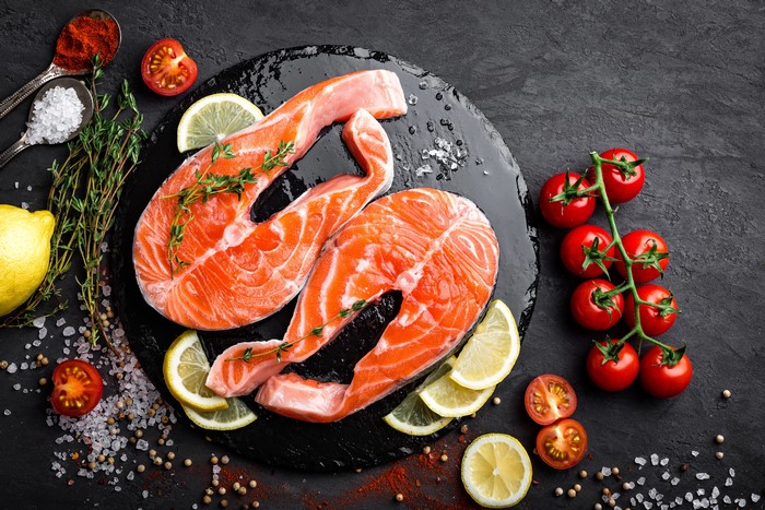 Salmon steaks with tomatoes, lemons, and herbs on a cutting board