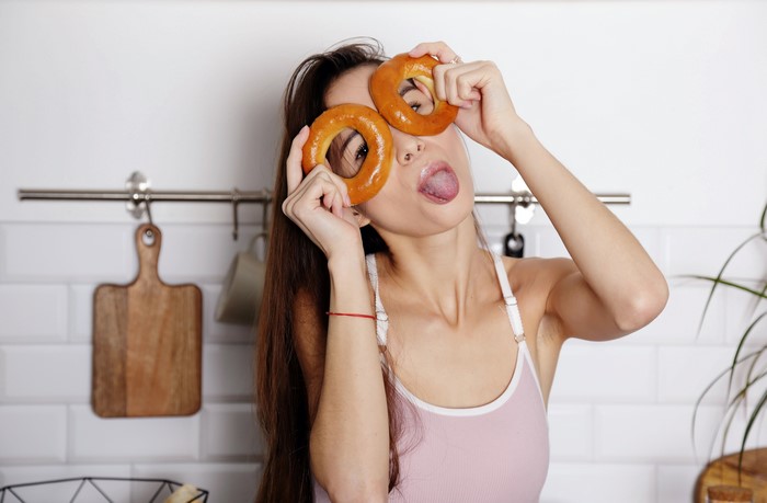 Woman holding bagels over her eyes