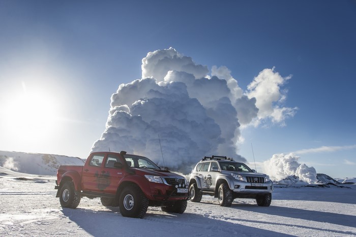 Two Arctic Trucks in Snowy Landscape with Volcanic Plume