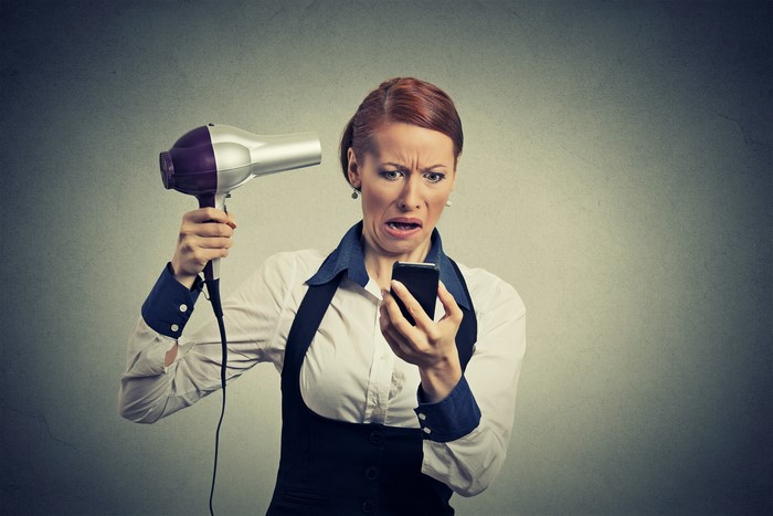 Woman with hairdryer and smartphone