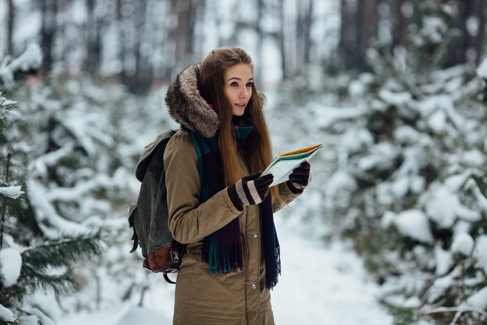 Woman with backpack holding a map in a snowy forest