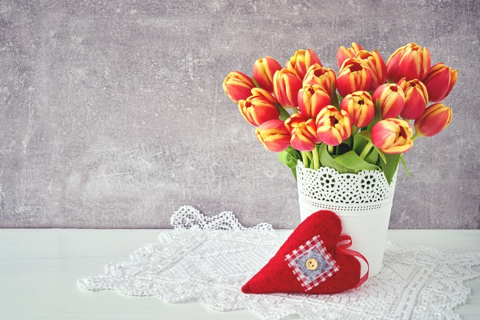 Red and yellow tulips in a white vase with a heart decoration