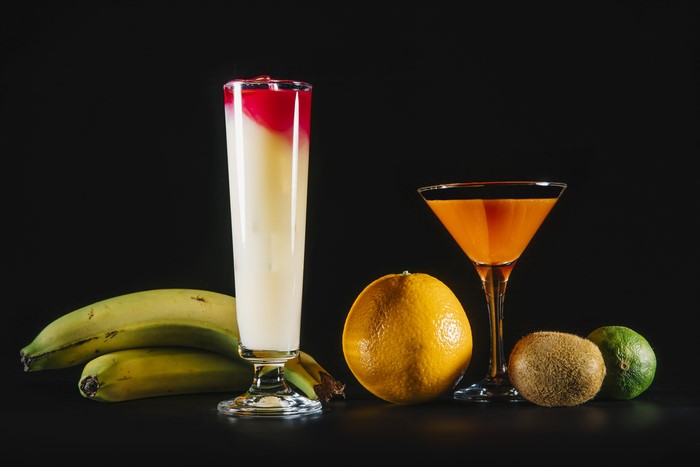 Two cocktails with bananas, orange, kiwi, and lime