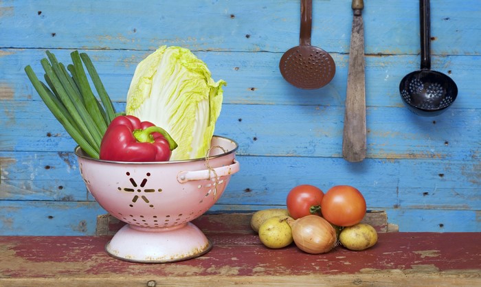 Vegetables in a colander on wooden planks