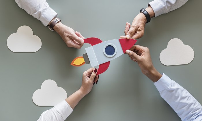 Hands holding a paper rocket with clouds