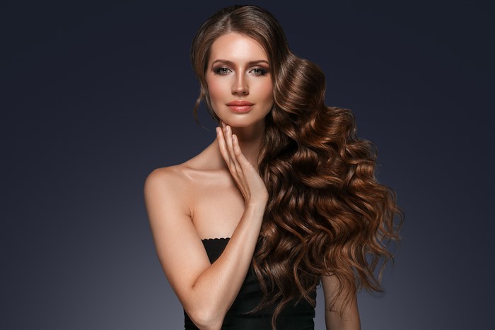 Woman with long curly brown hair and hand on face