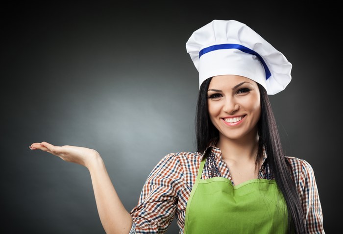 Brunette girl in chef hat and apron presenting something