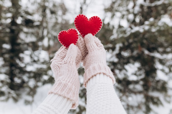 Two hands in mittens holding red hearts in winter
