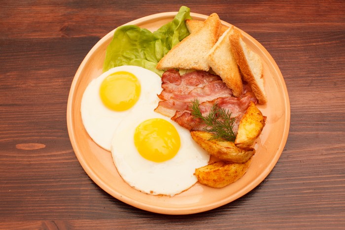 Breakfast plate with fried eggs, bacon, toast, and potatoes