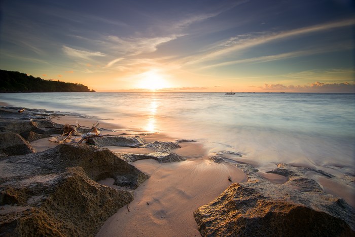 Sunset over the ocean with rocks on the shore